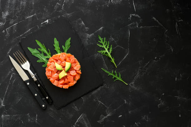 istock Fresh salmon, avocado and arugula salad in a culinary ring on a slate plate, black concrete background. Raw salmon tartare. Top view, flat lay, copy space. 1253505413
