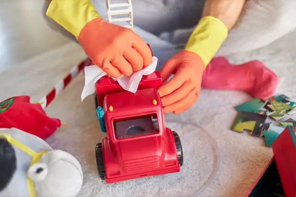 Photo of Various photos of a man disinfecting and cleaning children's toys with disinfectant wipes while wearing rubber gloves