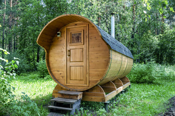 晴れた夏の日に森の中に丸い木製の樽風呂が立っています - サウナ ストックフォトと画像