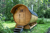 Round wooden barrel bath stands in the forest on a sunny summer day