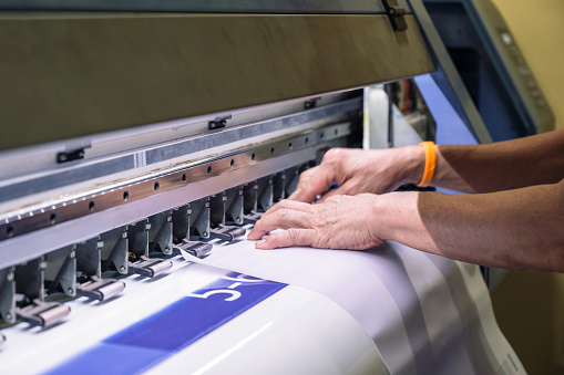 Hand technician catching a vinyl paper on large inkjet printer