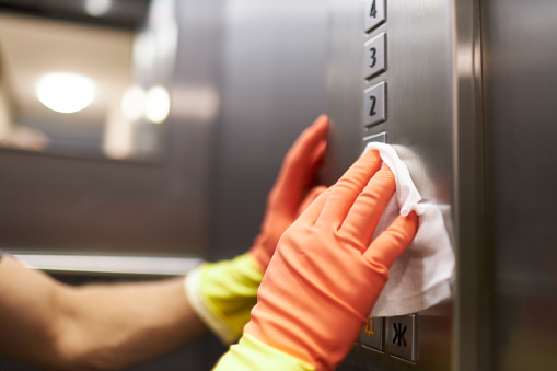 Different photos of a woman and a man disinfecting and cleaning an elevator with disinfectant wipes while wearing rubber gloves in the colors yellow and orange