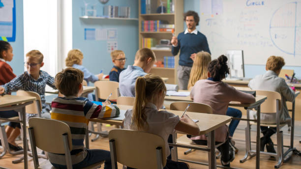 istock Caring Teacher Explains Lesson to a Classroom Full of Bright Diverse Children. In Elementary School with Group of Smart Multiethnic Kids Learning Science. 1253508031