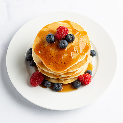 Overhead view of a stack of pancakes with blueberries and raspberries with syrup.
