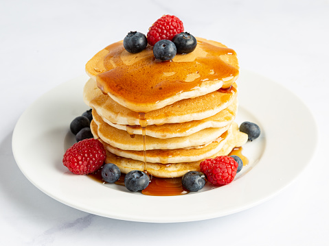 A stack of pancakes with blueberries, raspberries and syrup.