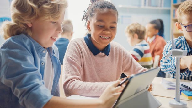 istock In the Elementary School: Girl and a Boy Work as a Team Using Tablet Computer. Diverse Classroom with Kids Learning Programming Language and Software Design 1253508062