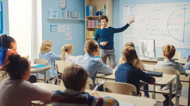 istock Caring Teacher Explains Lesson to a Classroom Full of Bright Diverse Children. In Elementary School with Group of Smart Multiethnic Learning Science, Listening to a Teacher with Great Interest 1253508117