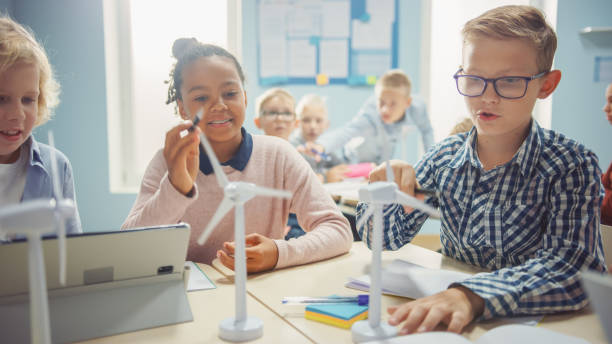 istock In the Elementary School: Class of Brilliant Young Children Work as a Team Using Tablet Computers to Program Wind Turbines. Classroom with Kids Learning about Eco-Friendly Forms of Renewable Energy 1253508683