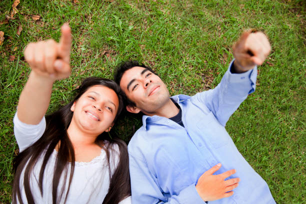 istock Happy couple lying down on grass pointing at the sky 1253508939