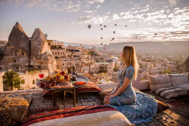 Woman is on the rooftop with standing view of Cappadocia. Balloons time on sunrise.