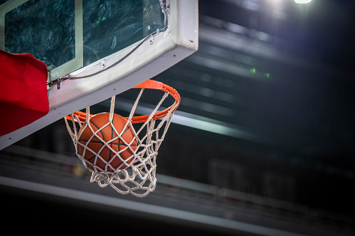 Close-up of basketball going through hoop in stadium.