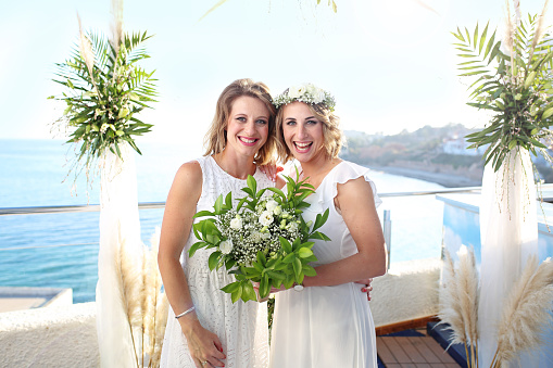 Bride in white gown, with flowers and happy expression on face at her spring wedding. Woman with bouquet of roses in her hands, smile and pose on day of her marriage ceremony with natural background