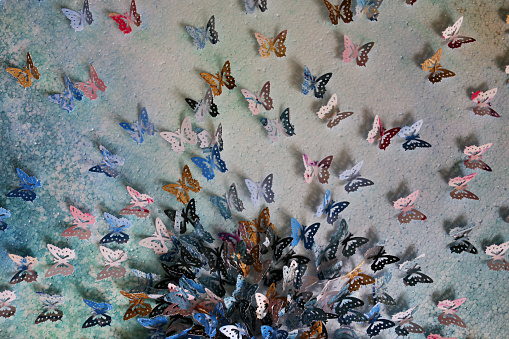 Stock photo showing homemade crafting art work with card and paper butterflies embossed and glued on abstract watercolour painting that has been painted on a stretched canvas. The butterflies were cut out using a butterfly design hole punch.