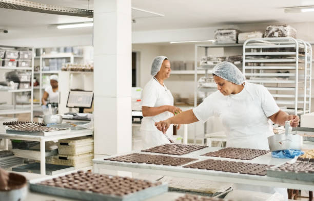 Professional chocolatiers working in chocolate factory Shot of a professional senior female chocolatiers preparing chocolates at confectionery shop hygiene in restaurant kitchen stock pictures, royalty-free photos & images