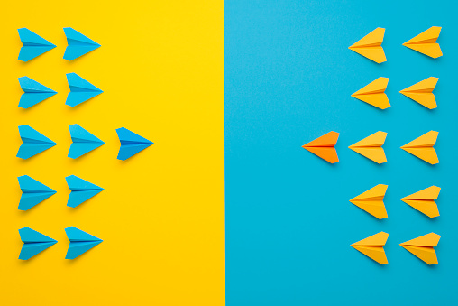 Paper airplanes teamed up in 2 colors, blue and yellow, face to face in battle formation. A confrontation between two teams, leading the team concept.