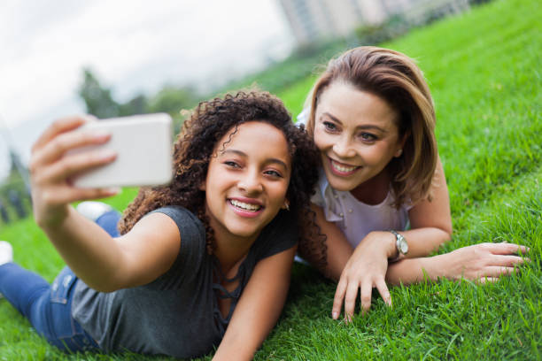 istock Young daughter taking a selfie with mom while relaxing on grass at the park 1253523484