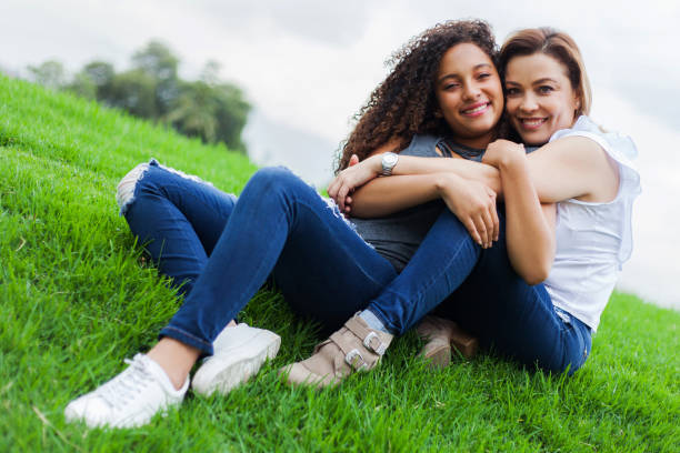 Mom and daughter hugging sitting on grass facing camera smiling very happy