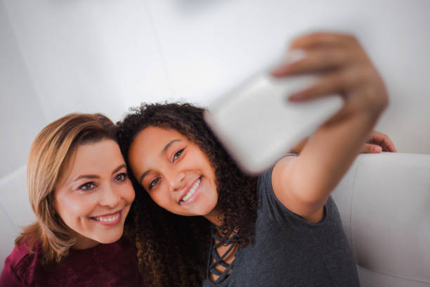 fille heureuse d’adolescence prenant un selfie avec sa mère tout en se relaxant à la maison - adoption early teens teenager family photos et images de collection