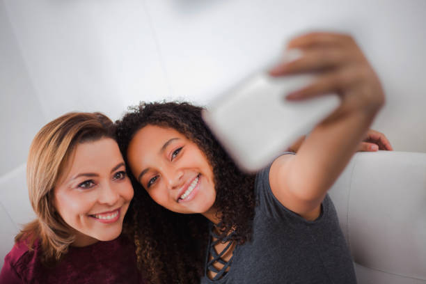 feliz filha adolescente tirando uma selfie com a mãe enquanto relaxa em casa - adoption early teens teenager family - fotografias e filmes do acervo