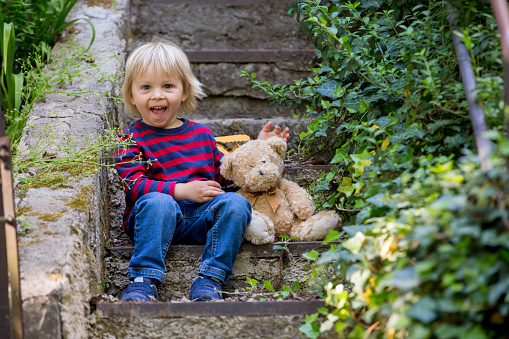Cute little todller boy, sitting on stairs with teddy bear