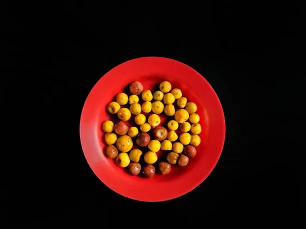 Photo of Yellow and brown nances on a red plate with a black background, typical fruit of Guatemala