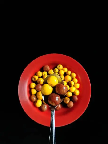 Photo of Yellow and brown nances on a red plate and a spoon with a black background, typical fruit of Guatemala