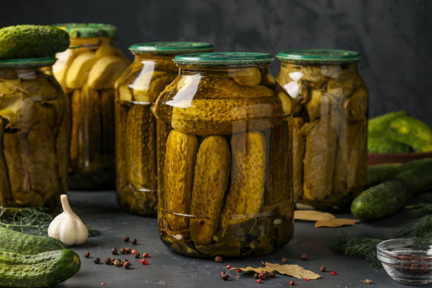 istock Different pickled cucumbers with zucchini, garlic and grape leaves in jars on a dark background, horizontal photo 1253525034