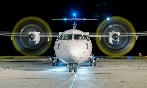 Photo of White commercial plane with engines running and propeller blur on a night with the moon on background