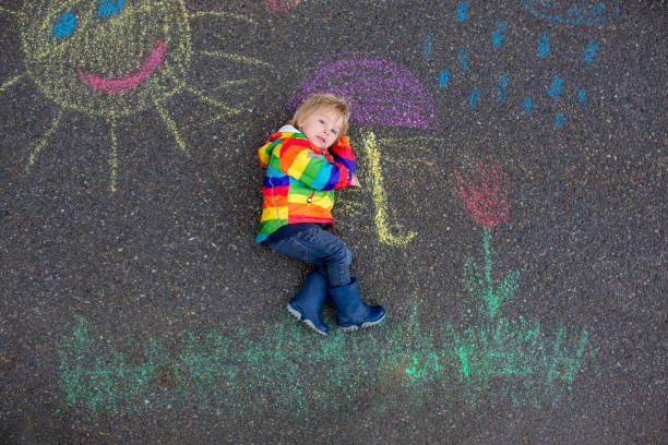 istock Cute toddler. playing in the rain with chalks, drawing on the asphalt, having fun 1253527962