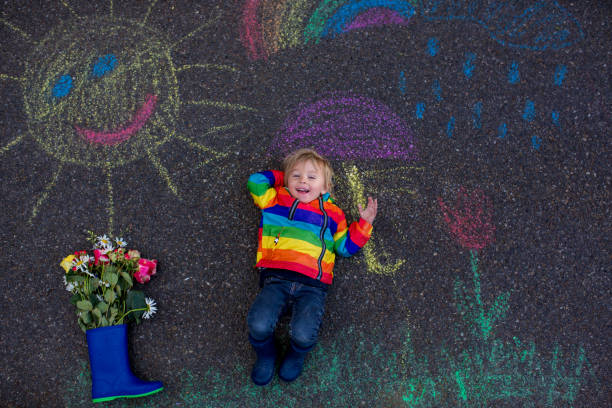 istock Cute toddler. playing in the rain with chalks, drawing on the asphalt, having fun 1253527978