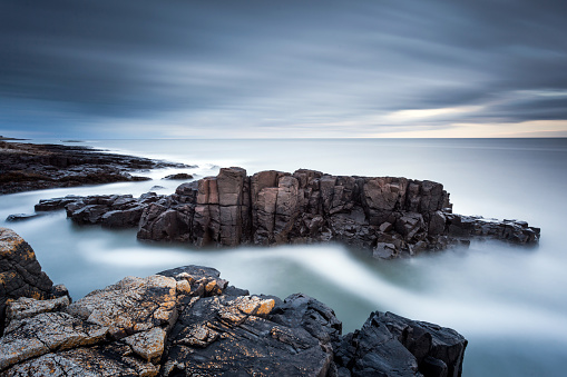 Long exposure seascape of a rocky coastline under a stormy sky, near Craster on the Northumberland coast, North East England.
