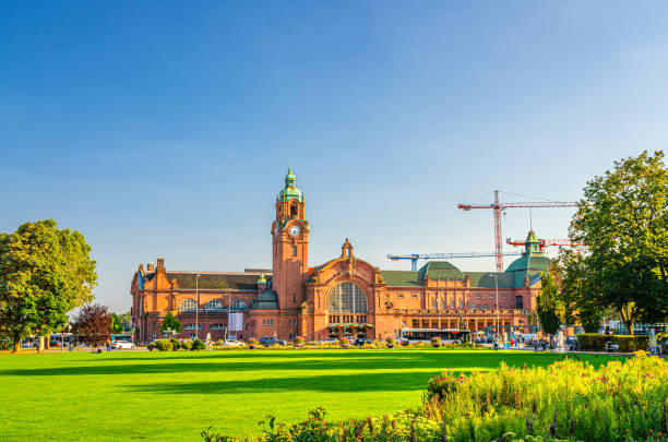 wiesbaden hauptbahnhof estación central de tren edificio de estilo neobarroco y parque reisinger-anlagen con árboles verdes y césped en el centro histórico de la ciudad, fondo del cielo azul, estado de hesse, alemania - neobaroque fotografías e imágenes de stock