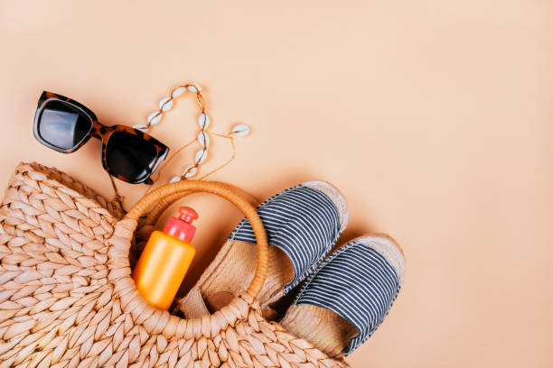 Summer fashion flatlay Summer fashion flatlay with summer straw bag, striped espadrilles sandals, sea shell necklace, sunscreen and tortoiseshell sunglasses isolated on beige background. beach bag stock pictures, royalty-free photos & images