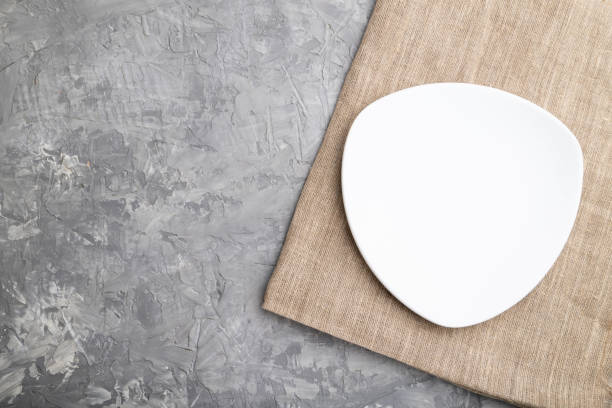 istock Empty white plate on gray concrete background and linen textile. Top view, copy space, flat lay. 1253540955