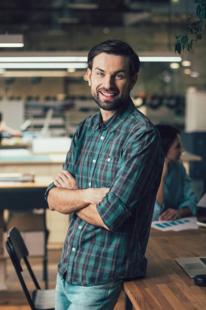 istock Contented young man standing by the table and smiling 1253541072