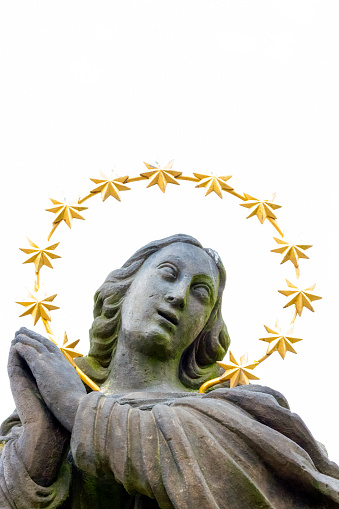 Closeup old statue of Virgin Mary with stars halo, white background with copy space, vertical composition