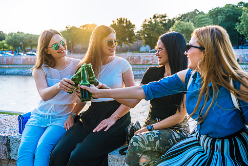 Four happy female friends toasting with beer bottles outdoors