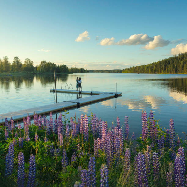 Two girls standing on a jetty at a peaceful lake on a summer evening.