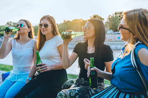 Four cheerful female friends drinking beer and chatting outdoors