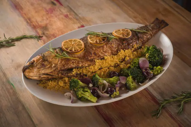whole roasted mullet, brocolles, onions and dehydrated orange slices, on wooden table