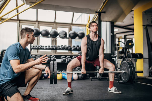 istock Fitness trainer helping a man in weightlifting training 1253547428