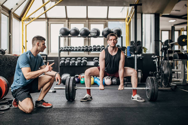 istock Fitness trainer helping a man in weightlifting training 1253547481