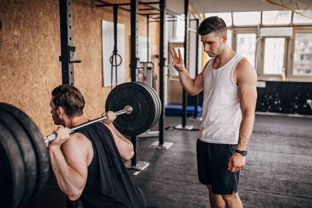 fitness trainer che aiuta un uomo nell'allenamento di sollevamento pesi - crouching barbell weightlifting weight training foto e immagini stock