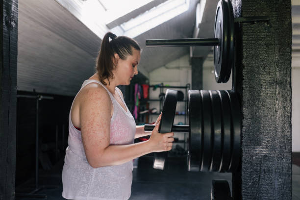 istock Strength Workouts: an  plus size Woman Taking a Disk Weight from the Rack 1253547636
