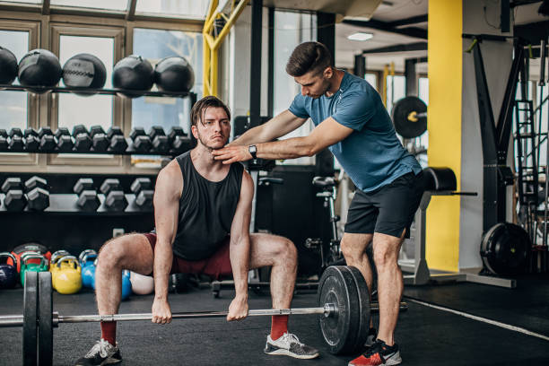 istock Personal coach helping a man in weightlifting training 1253547777
