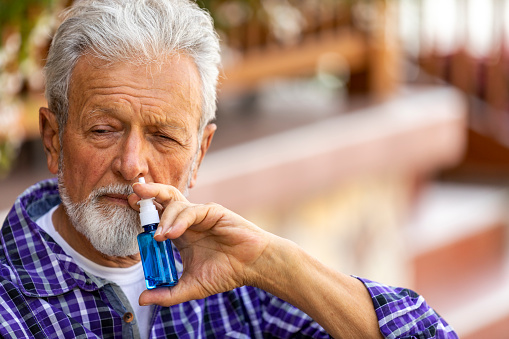 Senior Man is having flu and he is using nasal spray to help herself. Man using nasal spray. Nasal spray to help a cold. Sick with a rhinitis woman dripping nose. Man applies nasal spray