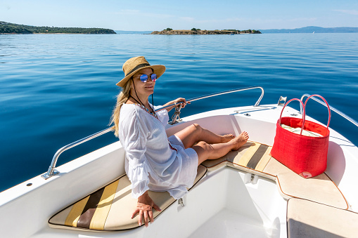 Adult woman with white pareo and sitting on yacht while travelling in the sea. Ouranoupoli, Greece.