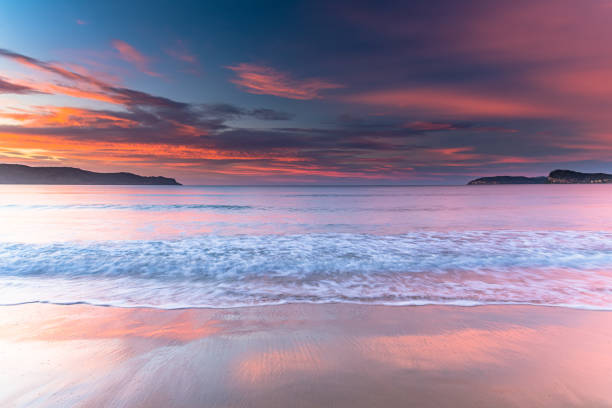 Early morning colors illuminate the sea and distant cliffs on Naxos, Greece, capturing soft waves and a glowing horizon in a tranquil coastal landscape.
