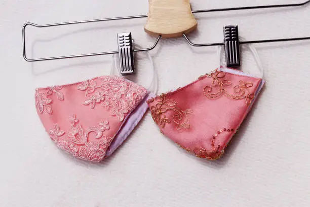 Photo of Pink lace reusable face masks hanging on clothes hanger placed on white background.