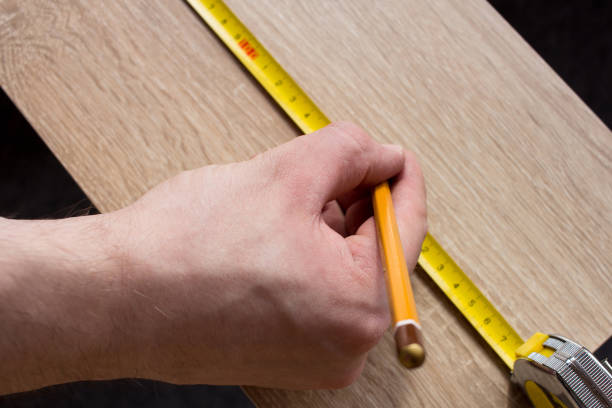 istock Man's hands measuring wooden plank with a tape line. 1253554792